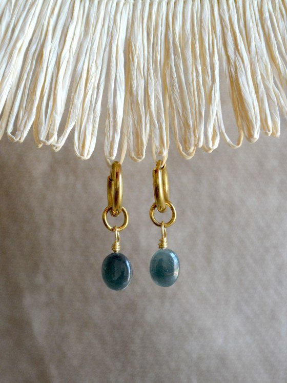 Aretes Belai Jade Princesa Pequeño, argollas de acero dorado con pequeño dije de piedra jade ovalada, apoyados sobre fibra de rafia y lino