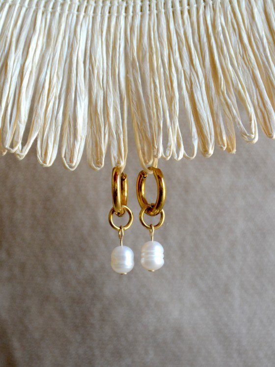 Aretes Belai Perla, argollas de acero con dije colgante de perla blanca, apoyados sobre fibra de rafia y lino