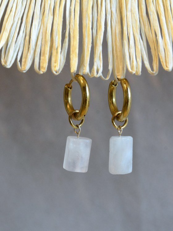 Aretes Belai Piedra Luna, argollas de acero con dije colgante de piedra luna blanca, apoyados sobre fibra de rafia y lino