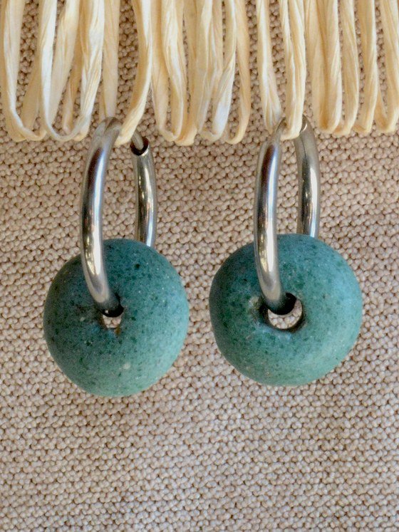 Aretes Belai Vidrio Esmeralda, argollas de acero plateado con cuenta de vidrio reciclado africano verde esmeralda en forma de disco, apoyados sobre fibra de rafia y lino