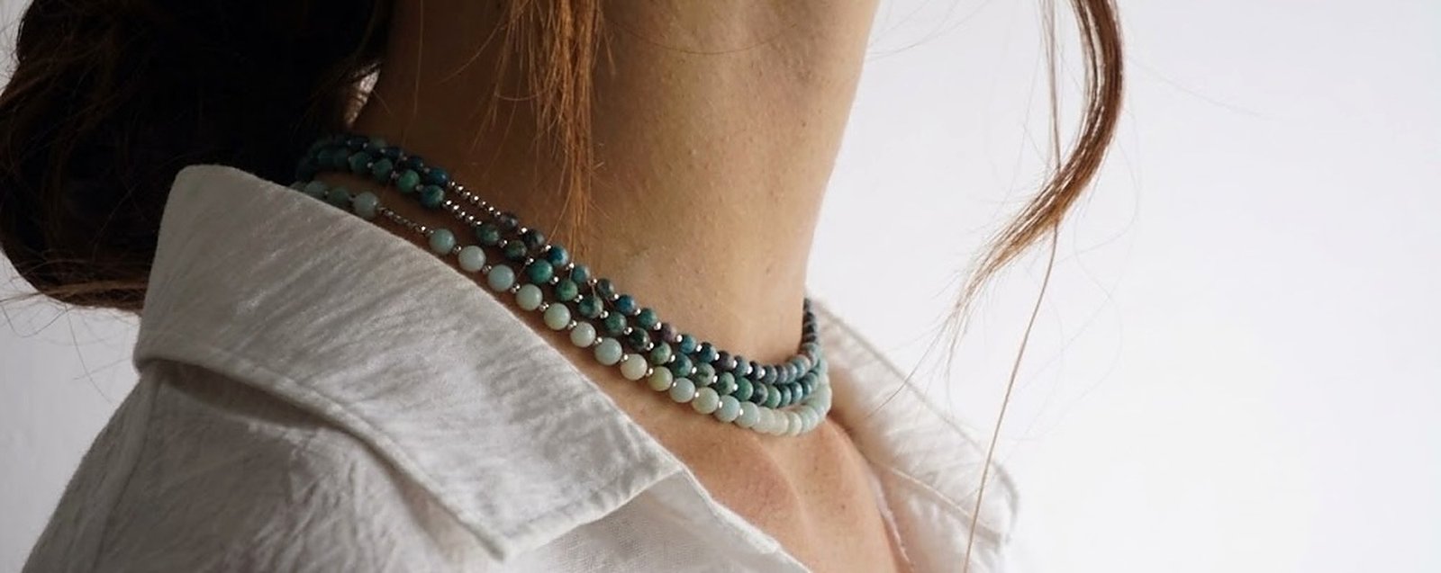 Primer plano de collares Belai de piedras naturales en capas alrededor del cuello: amazonita y apatita en tonos verdes y turquesas, sobre una camisa clara