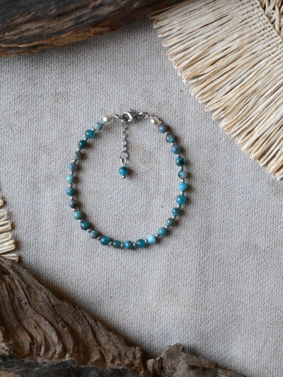 Pulsera Belai Apatita Plateada, cuentas de apatita azul con detalles plateados, apoyada sobre lino junto a madera y fibra natural