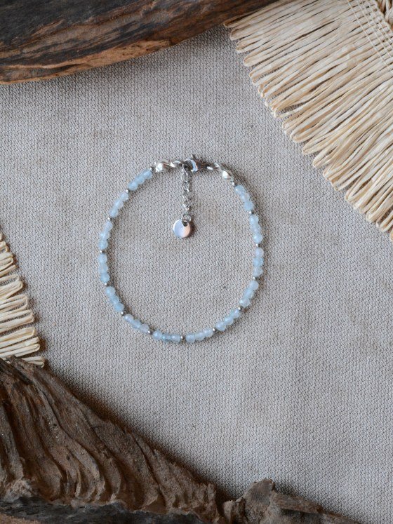 Pulsera Belai Aquamarina Plateada, cuentas facetadas color celeste aguamarina con detalles plateados, apoyada sobre lino junto a madera y fibra natural