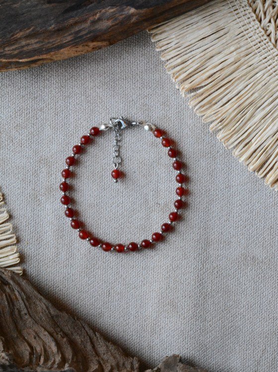 Pulsera Belai Cornalina Plateada, cuentas de cornalina roja con detalles plateados, apoyada sobre lino junto a madera y fibra natural