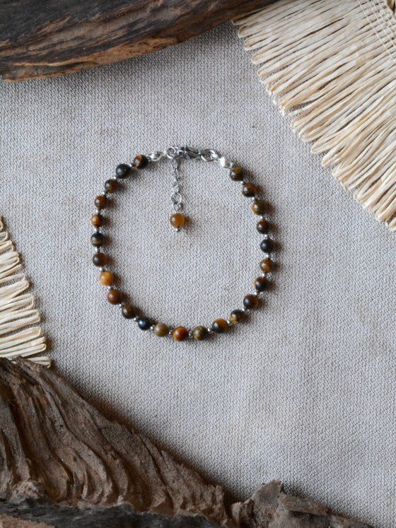 Pulsera Belai Ojo de Tigre Plateada, cuentas de ojo de tigre marrón dorado con detalles plateados, apoyada sobre lino junto a madera y fibra natural