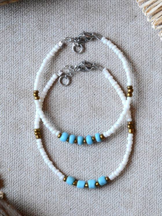 Pulsera Belai Turquesa y Blanco Plateada, cuentas blancas con turquesa celeste y detalles plateados, apoyada sobre lino junto a madera y fibra natural